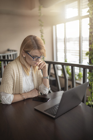 Young nervous business woman using her laptop computer in restaurant. Blonde attractive woman working on her laptop computer in coffee shop, solving business problems.の写真素材