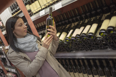 Woman in store deciding what wine to buy. Young woman choosing and buying wine in market or liquor store. Sale, shopping, consumerism and people concept.の写真素材