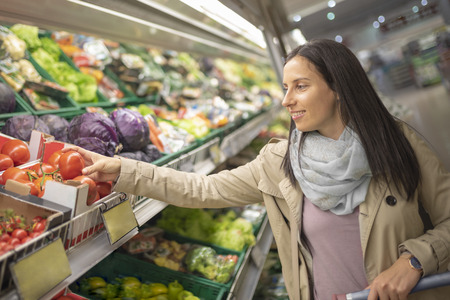 Pretty young woman picking up, choosing green leafy vegetables in grocery store. Attractive woman shopping in supermarket. Shopping woman buying healthy food. Healthy lifestyle concept.の写真素材