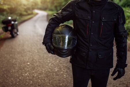 Motorcycle guy in raiders clothes, gearing up. A young men stands near an motorcycle in nature during sunset. Biker with motorcycle on the road. Motorcycle and safe driving. Helmet and motorcycle.の写真素材