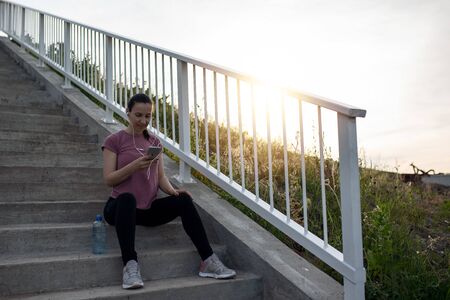 Sunset exercise with beautiful, sport woman. Woman fitness jogging, workout wellness concept. Female runner listening to music while joggingの写真素材