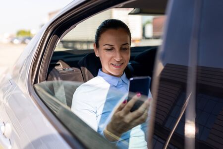 Business woman sitting in the car and looking at the cell. Business woman in a car on the phone. Beautiful business woman in the car. Business and lifestyle concept.の写真素材