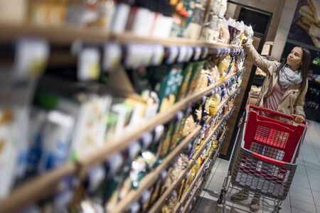 Housewives, women with shopping cart in supermarket. Closeup portrait of beautiful and pretty young woman picking up and choosing products in supermarket.の写真素材