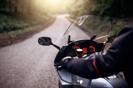 Driver riding motorcycle on the road through forest. Biker with his motorcycle on street, preparing for the ride. の写真素材