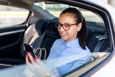 Business woman sitting in the car and looking at the cell. Business woman in a car on the phone. Beautiful business woman in the car. Business and lifestyle concept.の写真素材