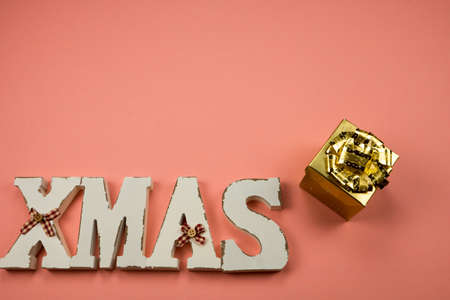 Christmas greeting card on pink background. Write Xmas and golden gift. Space for textの写真素材