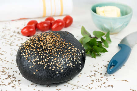 Black bun bakery with sesame. Served on rustic white wooden table with butter and tomatoes. Black bakery can be replacement for common white meal products. Ideal for interesting burgers.の写真素材