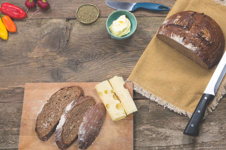 Homemade rye bread served on wooden table with cheese, butter and fresh vegetables.の写真素材