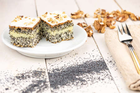 Poppy cake with creamy filling and walnuts on the top of dessert. Served on white wooden retro table and golden form in warm colors. Poppy in the Slovak republic is legal plant.の写真素材