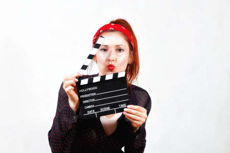 Young redhead happy pin up girl in bandana and black shirt with red lips kissing through movie clapperの写真素材