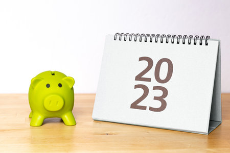 2023 calendar and piggy bank on the wooden desk with white background