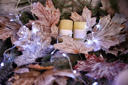 Christmas decorations two candles lie on dried maple leaves and Christmas tree branches with garland of light bulbsの写真素材