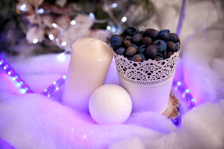 Christmas scenery white candle on the side and snow ball near white bucket with acornsの写真素材