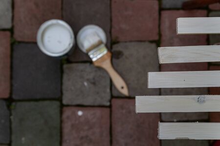 paint brush covered with white paint in hand and paint can paint wooden planks on the dark background in the yardの写真素材