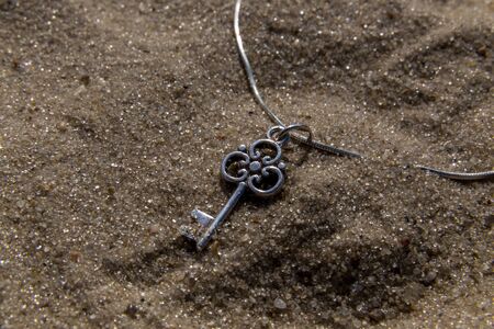 silver pendant key close up on sand on the beach on a sunny dayの写真素材