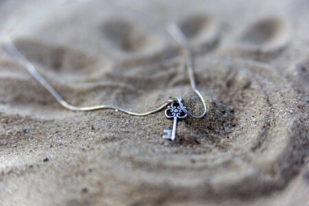 silver pendant key close up on sand on the beach on a sunny dayの写真素材