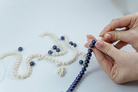Close-up of hand of needlewoman making necklace of natural pearlsの写真素材