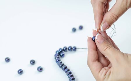 Close-up of hand of needlewoman making necklace of natural pearlsの写真素材