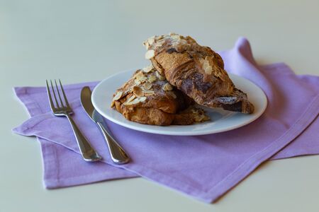 croissants with chocolate and almond on a white plate and purple napkinsの写真素材