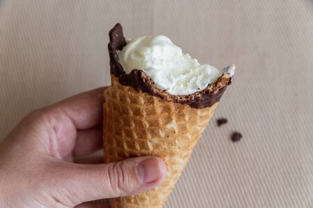vanilla ice cream in wafer cup bitten in hand