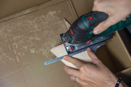 man cuts a wooden board with a jigsaw on a cardboard box at home handmadeの写真素材