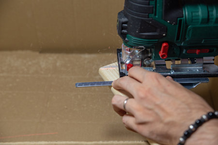 man using electric jigsaw at home to cut piece of wood board on a cardboard box. Do it yourself.の写真素材