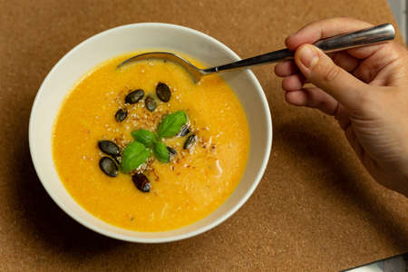 spoon in hand dipped in a plate with pumpkin cream soupの写真素材