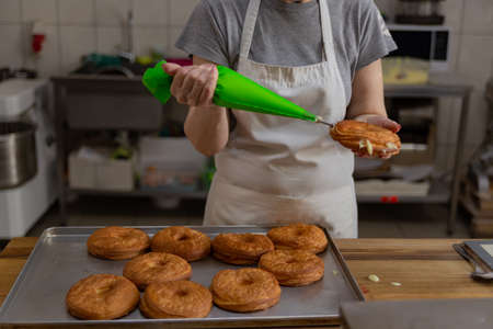 confectioner fills donuts with vanilla creamの写真素材