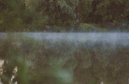 morning fog on the lake in the morning at sunrise the trees are reflected in the waterの写真素材