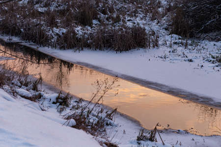 view of a stream in the water reflects the golden sky from the sunset in winterの写真素材