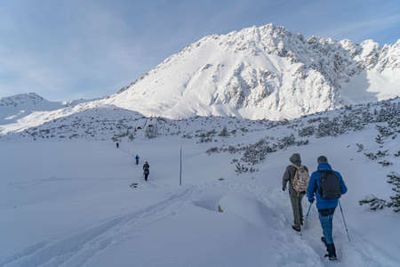 Tatra Mountains, Winter mountain landscape in the Tatras, tourists climb the snowy slopes, views of the snow-capped mountains in frosty sunny weatherの写真素材