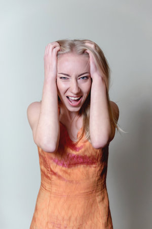 beautiful blonde woman angry and annoyed in pain from stress looks straight into the camera dressed...