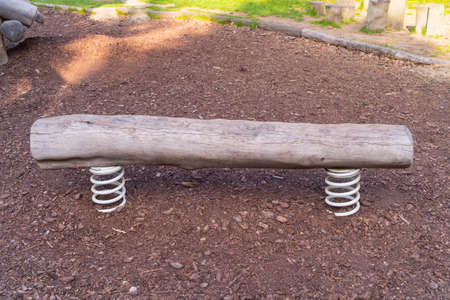 a wooden bench made of a tree trunk on metal white springs on the ground covered with shredded bark from trees, front photo, the bench is not covered with anything, dry in the parkの写真素材