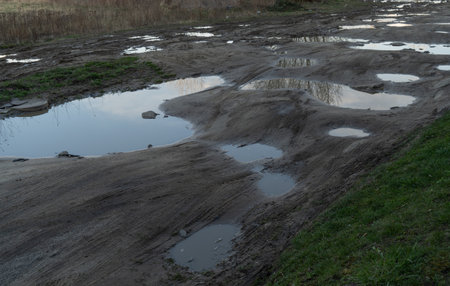 Muddy puddle road after rain with big puddles in the city