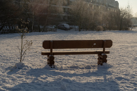 wooden bench in the park covered with snow in sunny weather on a frosty winter dayの写真素材