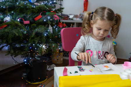 a little girl makes and decorates New Year's decorations with colored paper and with sparklesの写真素材