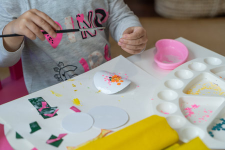 little child makes decorations from colored paper with glue and scissors and paint brush top view on work surfaceの写真素材