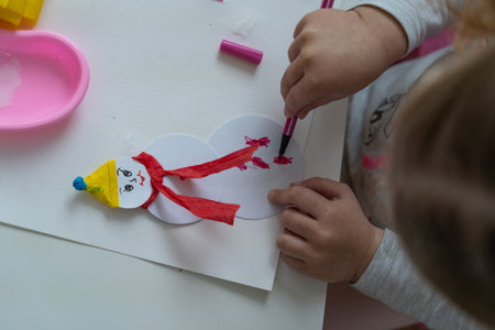 little child makes decorations from colored paper with glue and scissors and paint brush top view on work surfaceの写真素材