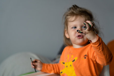 a happy little girl paints her hand with colored paints a girl in an orange blouse with a giraffeの写真素材