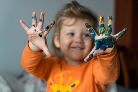 a happy little girl paints her hand with colored paints a girl in an orange blouse with a giraffeの写真素材