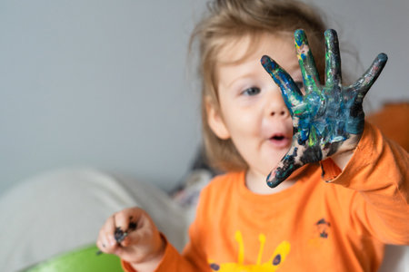 a happy little girl paints her hand with colored paints a girl in an orange blouse with a giraffe