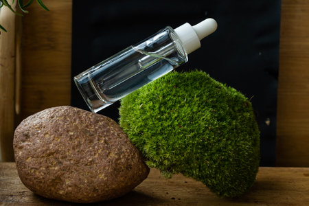 glass transparent bottle with natural cosmetic product and dispenser on moss, stone, tree and black backgroundの写真素材