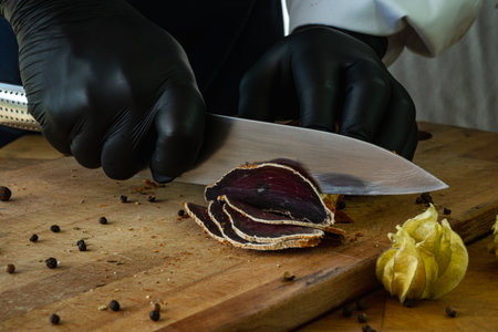 A chef in black gloves cuts basturma on a wooden board