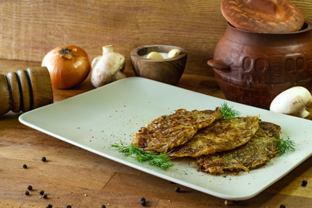 Fried potato pancakes with mushrooms on a white plate on a wooden backgroundの写真素材