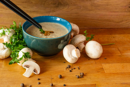 Mushroom soup in a blue bowl with parsley and mushrooms Chef's hands serve the soupの写真素材