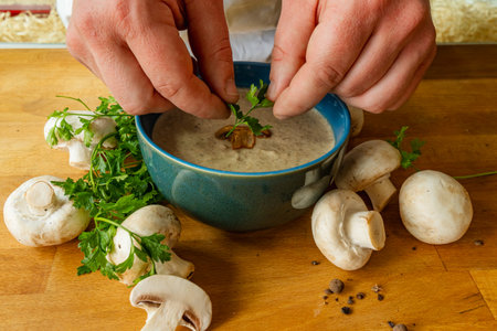 Mushroom soup in a blue bowl with parsley and mushrooms Chef's hands serve the soupの写真素材