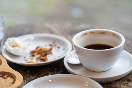 An after-meal scene with an empty coffee cup, a crumpled napkin, and croissant crumbs on a wooden tray and a white plate.の写真素材