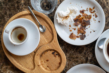 An after-meal scene with an empty coffee cup, a crumpled napkin, and croissant crumbs on a wooden tray and a white plate.の写真素材