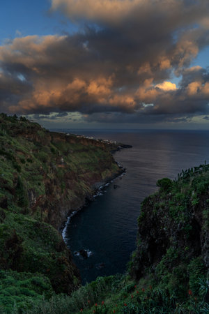 A serene view of a rocky coast with red flowers, under a dusk sky with fluffy clouds Colorful sunset at CaniÃ§o, Madeira island, Portugalの写真素材