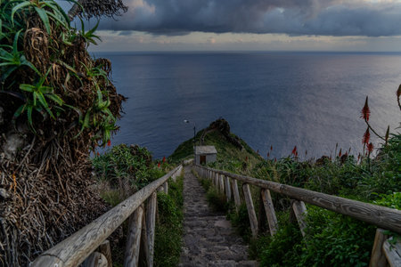 a view of the stairs with a wooden railing towards the ocean rocky coast , under a dusk sky with...